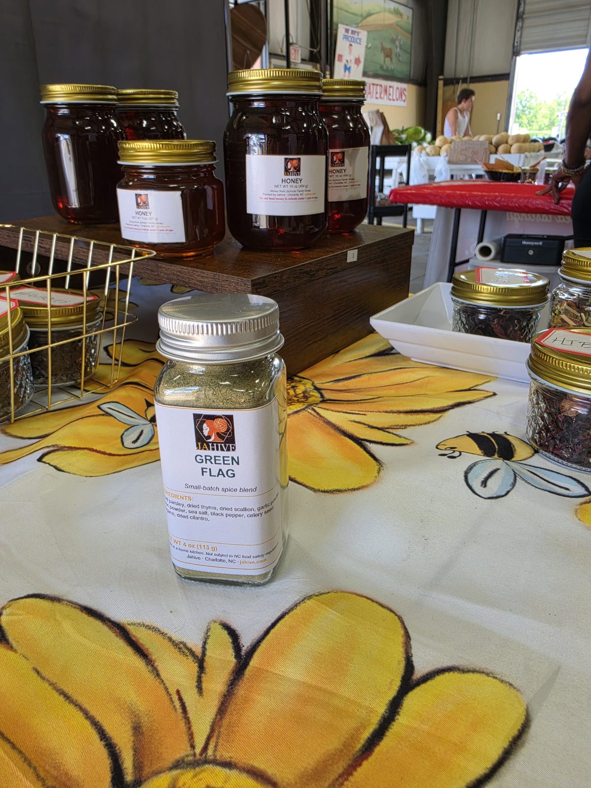 The Jahive booth at the Charlotte Regional Farmers Market with honey jars and spice blends on a sunflower tablecloth
